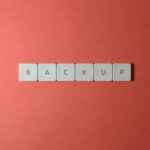 Free Close-up of keyboard keys spelling 'BACKUP' placed on a coral-colored surface. Stock Photo